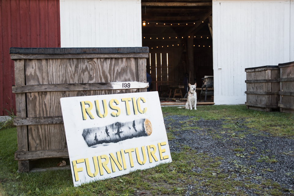 Image of sign, barn, with dog sitting in front.