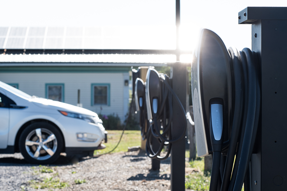 Car plugged into electric vehicle chargers in front of solar panels.