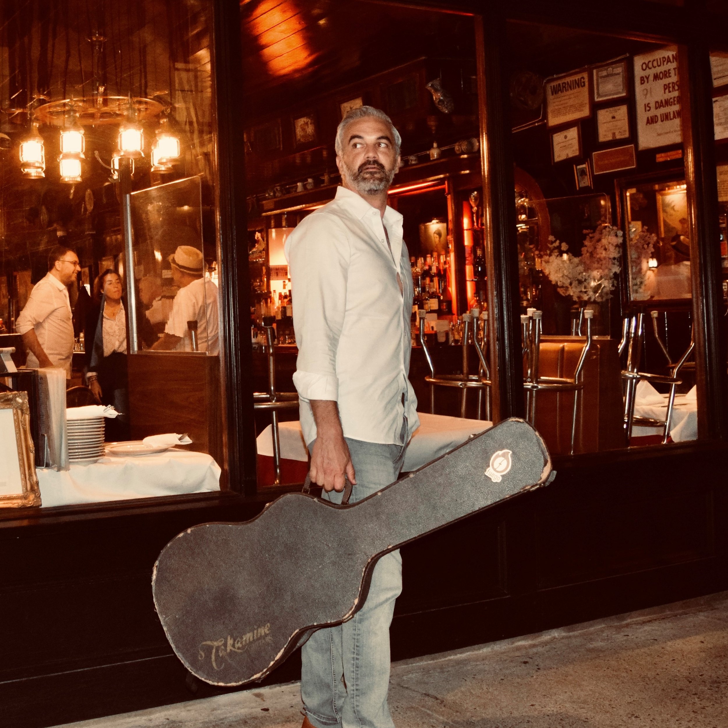 Portrait of Daniel King standing on a sidewalk with guitar case in hand.
