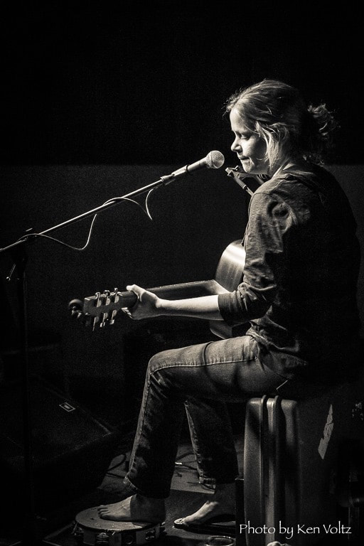 Laura Thurston sitting and singing with a guitar and harmonica