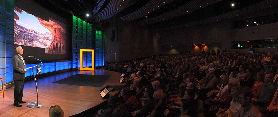 Image of person presenting film to a theater full of people.