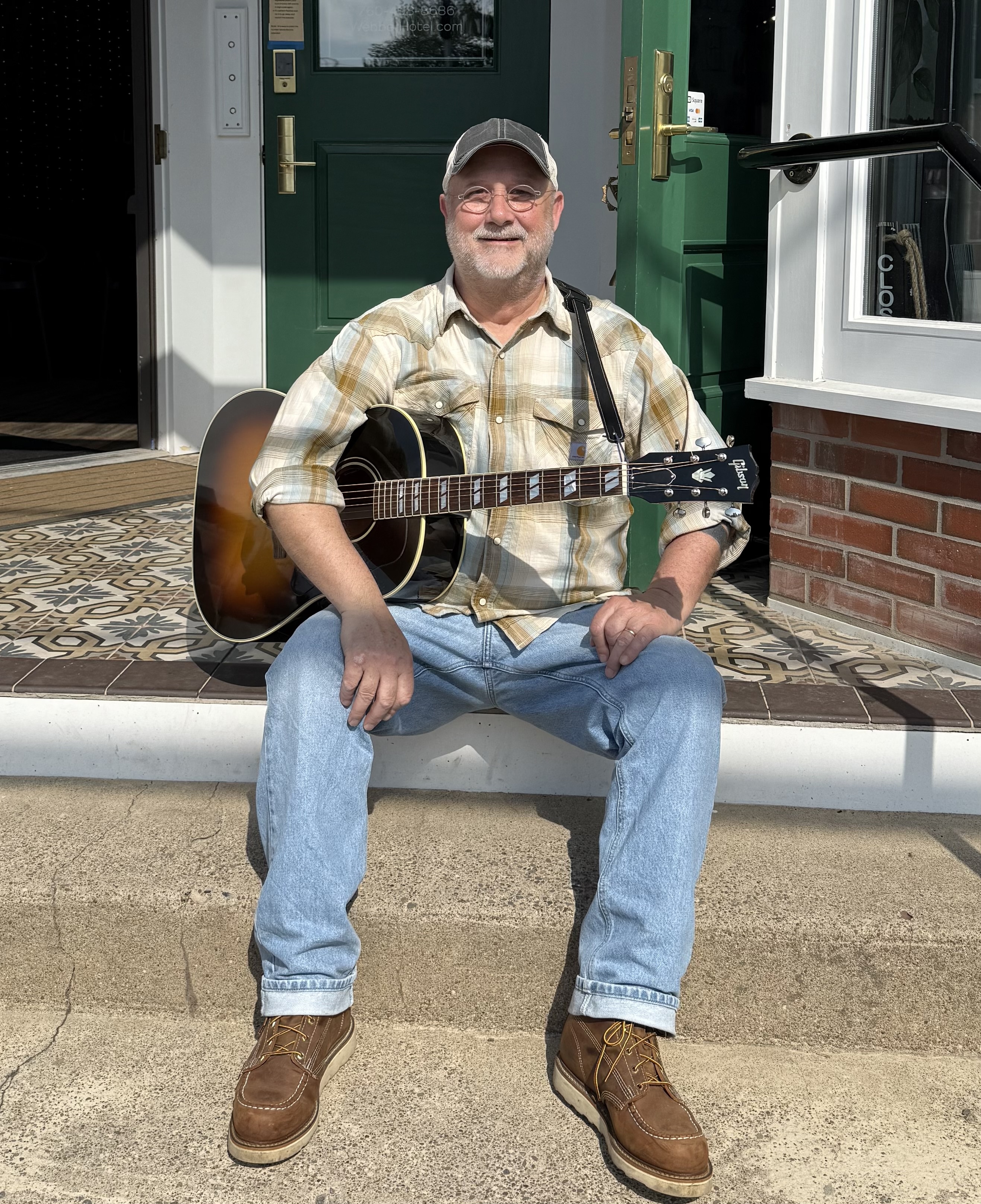 Portrait of Tom Keil sitting on outdoor stairs with his guitar